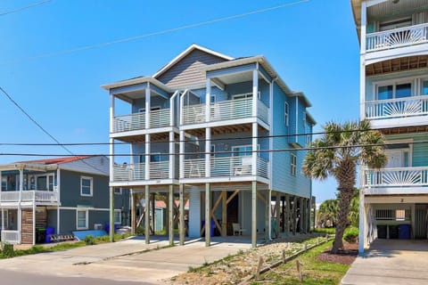 Coastal beach house with elevated design, featuring wraparound balconies and modern architecture nestled in a palm-lined residential neighborhood.