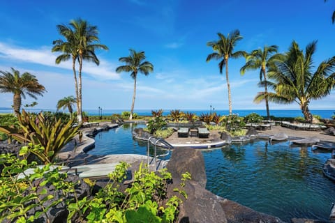 Tropical oceanfront pool oasis with volcanic rock accents, swaying palms, and stunning sea views, offering a tranquil setting for relaxation and leisure.