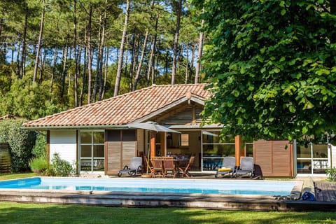 Stone-and-timber villa with a private pool in the garden — tall Landes pines rising behind, the lake a short walk away.
