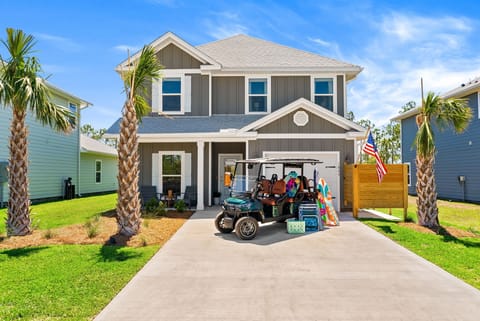 A modern two-story coastal-style home nestled in a welcoming neighborhood, framed by palm trees and featuring a covered porch and spacious driveway, ready for your beach getaway adventures.