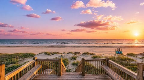 Sunset Gulf view from the beach access stairs, featuring sandy shoreline, ocean waves and a colorful sky at this Port Bolivar beach vacation rental.