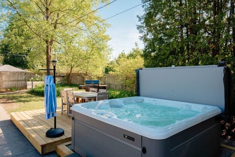 An outdoor backyard scene featuring a large hot tub, a dining area, and lush greenery. 🌳