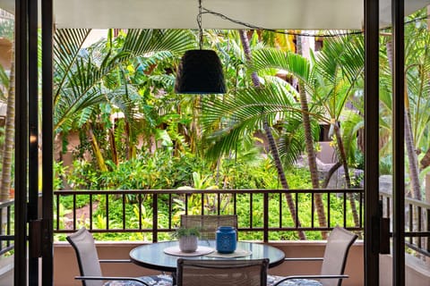 Balcony table and chairs rest in greenery, hanging light glowing above palms.
