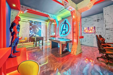 Welcome to a vibrant superhero haven, where bold colors and striking decor ignite your imagination. Enjoy the playful game room with sleek chairs, an Avengers mural, and dynamic lighting for the ultimate fun atmosphere.