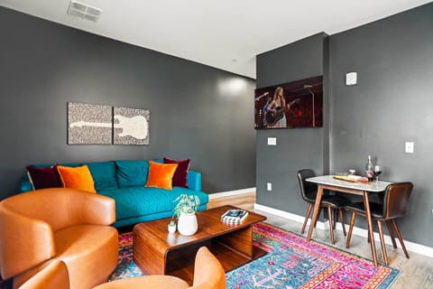 The living area brings bold personality with a teal sofa, leather swivel chairs, a sculptural wood coffee table, vibrant area rug, music-inspired art and a large smart TV.