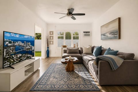 Spacious coastal living room with large sectional sofa, ceiling fan, and wall-mounted TV — the perfect place to unwind after a day at the beach three minutes away