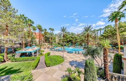 Clubhouse view of the resort style pool with hot tub, cabanas, and palm trees.