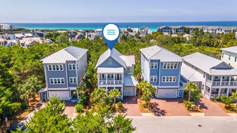 A coastal neighborhood of modern vacation homes with turquoise Gulf waters just beyond, nestled among lush greenery and palm trees.