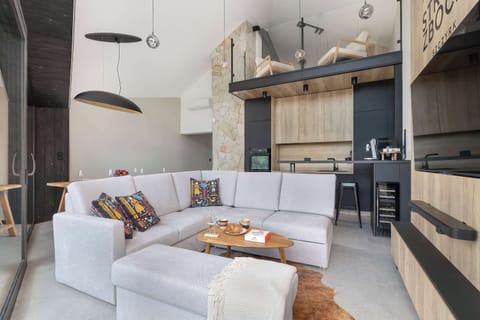 A modern living room connected to a compact kitchen with wooden furniture and stylish lighting. The interior feels cozy and contemporary.