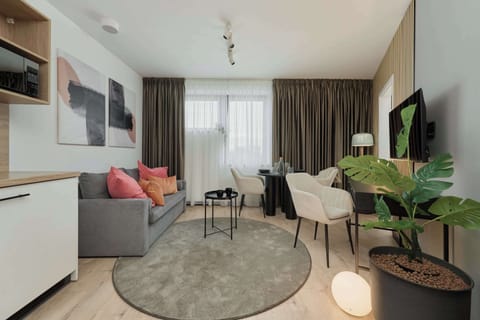 A stylish living room with a gray sofa, coral accent pillows, a modern rug, and lush green plants.

