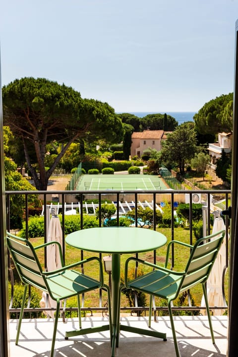 Round green table and chairs on the balcony with the pool, tennis courts, and park spread below