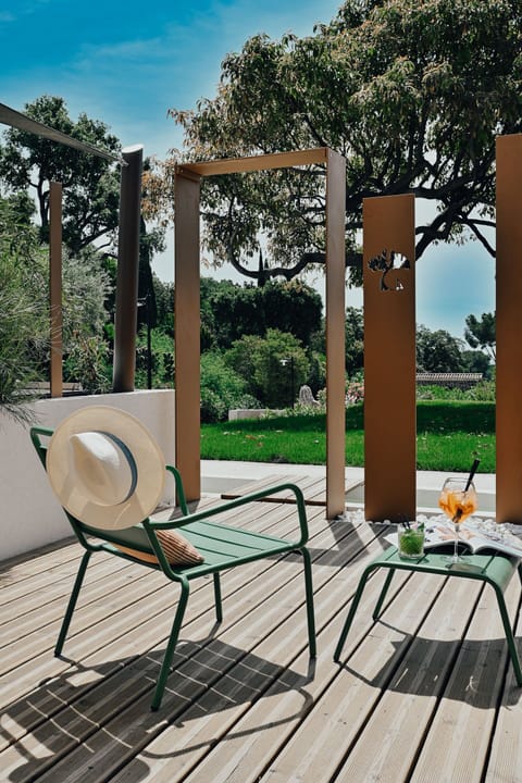Green metal chairs and a small table on the private shaded terrace, surrounded by garden trees