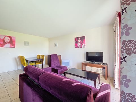 Living area with purple sofa, black coffee table, and yellow dining chairs — sofa converts to a double bed