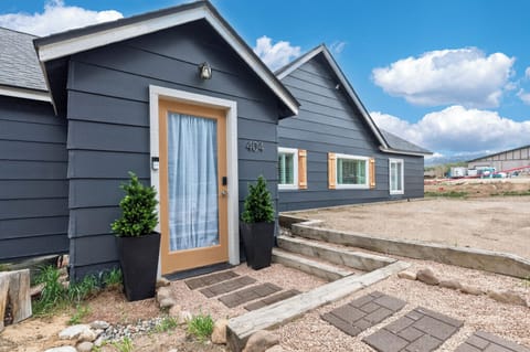 Modern charcoal-gray vacation home with mountain views and a welcoming wood-framed entrance. The property is set in a developing neighborhood with natural landscaping and tiered stone walkways.