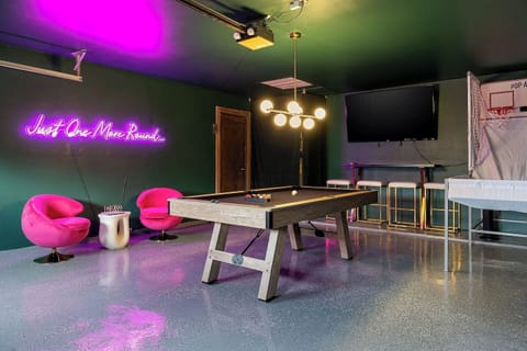 Step into a vibrant game room featuring a pool table, modern bar stools, a large smart TV, and eye-catching neon wall art. There is a Pop-A-Shot, table top games, and a hook game for everyone to have fun!