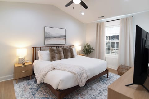 The primary bedroom offers a king-sized Purple mattress with luxe linens and blackout curtains, along with a smart TV, full-length mirror, luggage rack, and closet storage with hangers and a dresser.