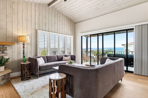 Bright ocean-view living room with vaulted ceilings, cozy seating, and seamless access to the balcony.