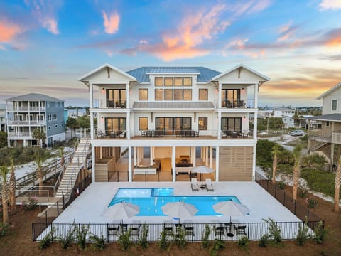 A stunning three-story coastal retreat features a private pool, covered porches, and panoramic sunset views, perfectly positioned near the beach in a peaceful neighborhood.