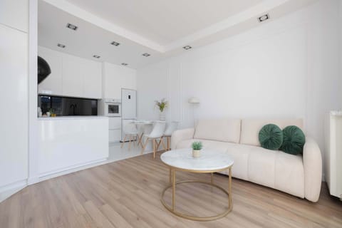 A stylish open space featuring a white sofa and a round coffee table next to a contemporary kitchen. The design emphasizes simplicity, light colors, and functionality.