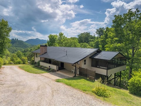 Welcome to Rocky Top Retreat - Front exterior of the cabin showing the gravel driveway approach, front covered porch, screened porch addition, and mountain view behind.