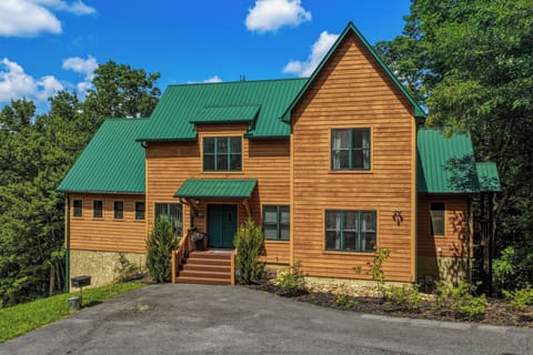A charming wood-sided retreat with a distinctive green metal roof, nestled among tall trees in a peaceful, natural setting with convenient paved parking.