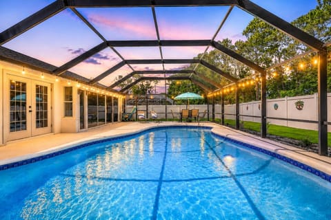 Twilight poolside evenings at Whispering Waves Retreat with screened enclosure, loungers, and outdoor dining under the coastal sky.