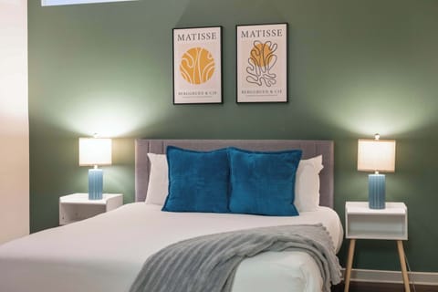 Cozy bedroom with sage green accent wall, warm lighting, and plush bedding with blue throw pillows.