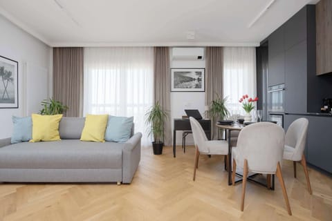 A bright studio apartment with a bed, dining table, and kitchenette in one open space. Large windows provide plenty of natural light.