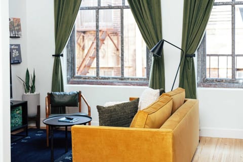 A warm, modern retreat with high ceilings, green drapes, and a golden sofa made for lounging
