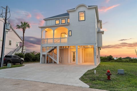 Waterfront beach house exterior with sunset skies, elevated architecture and oversized driveway near Galveston Bay.