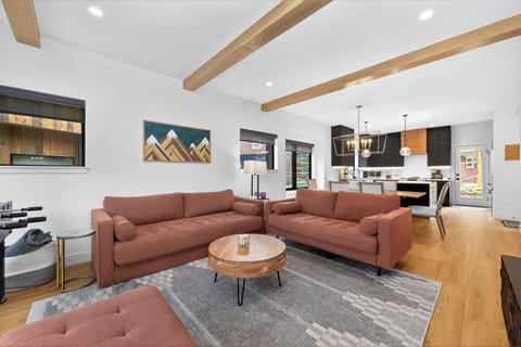 Sink into plush sofas in your open-concept living space with mountain art and exposed beams, flowing seamlessly into a sleek kitchen perfect for your vacation cooking.