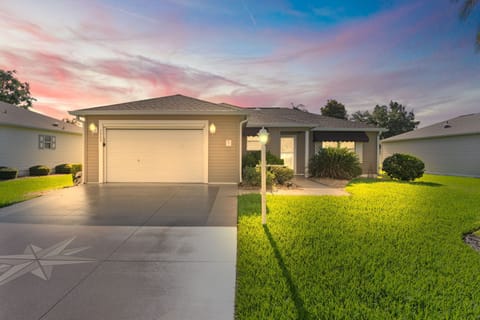 Single-story vacation home situated in a peaceful residential neighborhood, captured at dusk with illuminated exterior lighting and well-maintained landscaping enhancing its welcoming presence.