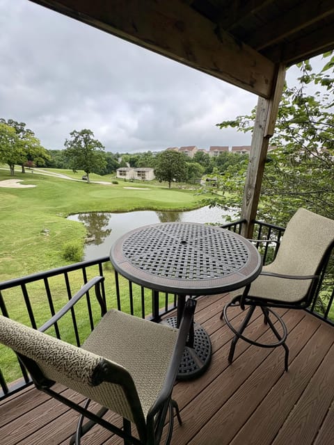 Covered balcony with patterned metal table and cushioned chairs overlooking golf course pond and green fairway.