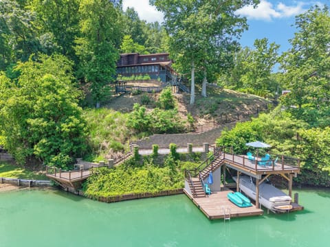 Elevated lakefront property featuring a private dock, outdoor seating areas, and scenic wooded surroundings.