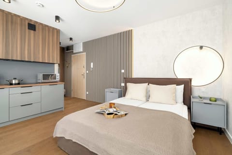 A modern studio bedroom with a comfortable double bed and a clean, minimalist design. The space includes warm wooden accents and a compact kitchen area for added convenience.