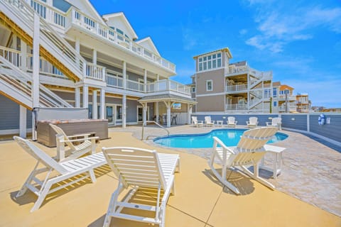 This stunning coastal retreat offers an expansive pool deck where you'll soak up the sun on comfortable loungers, surrounded by elegant coastal architecture under brilliant blue skies.
