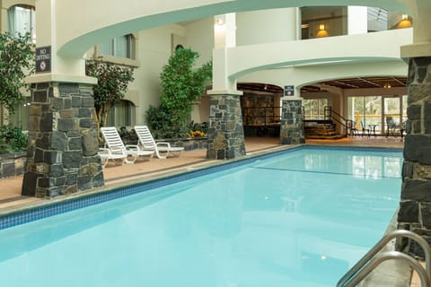Indoor pool lined with grey stone columns and white lounge chairs under a two-story atrium