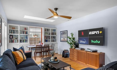 Open-concept living and dining great room with a navy sectional, Smart TV, and skylight keeping the group connected.