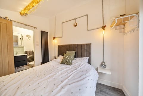 Cosy double bed with industrial pipe lamps and a glittering chandelier above.