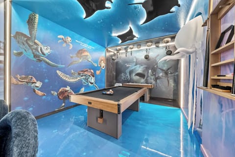 Immerse yourself in a lively game room adorned with a beautiful ocean-themed mural, where the glossy blue floor reflects the marine art and a sleek pool table awaits to inspire friendly competition among guests.
