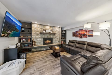 Leather sectional curves around a dark wood coffee table, facing a stone fireplace and wall-mounted TV.