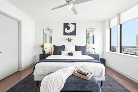 King bed with hotel-style linens, hardwood floors, and floor-to-ceiling windows with city views.