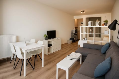 Modern living area with a gray sectional sofa and a white dining table for four.