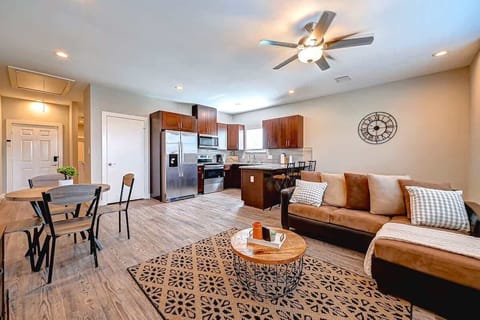 Stylish open-concept living space featuring a modern kitchen with stainless steel appliances, a cozy living area with a sofa and accent rug, and a round dining table. Warm tones and thoughtful decor create an inviting, functional atmosphere