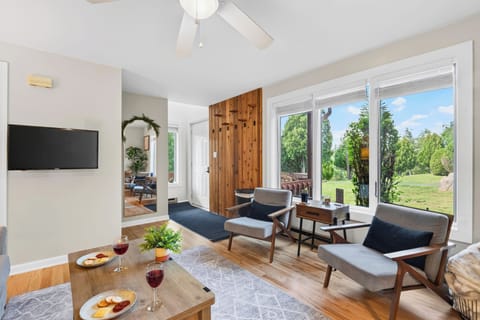 Natural light pours into the living room, where oversized windows, comfortable seating, and a wall-mounted TV create an easy place to unwind.