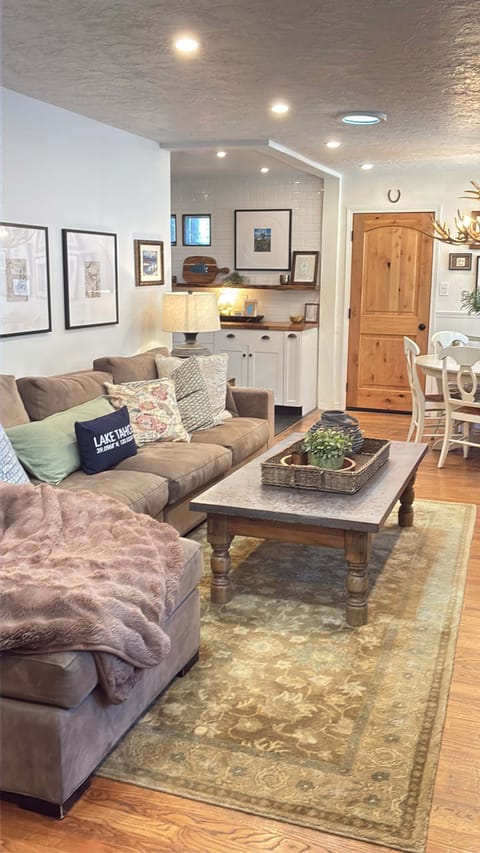 Living area with sofa chaise, coffee table, side table, lamp, dining table, window bench, and front door.