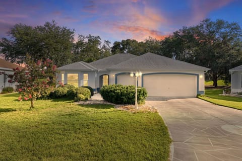 A charming single-story home framed by lush mature trees and landscaping, set in a peaceful neighborhood with vibrant sunset skies overhead.