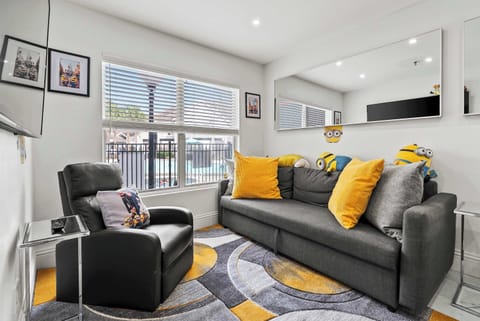 Bright living room w/ plush gray sofa, yellow accents, & large windows that fill the space w/ natural light.
