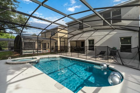 Screened pool area with clear blue water, adjacent spa, black mesh safety fence, and two lounge chairs.