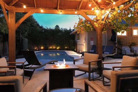 Covered poolside lounge with fire table, string lights, and cozy evening ambiance